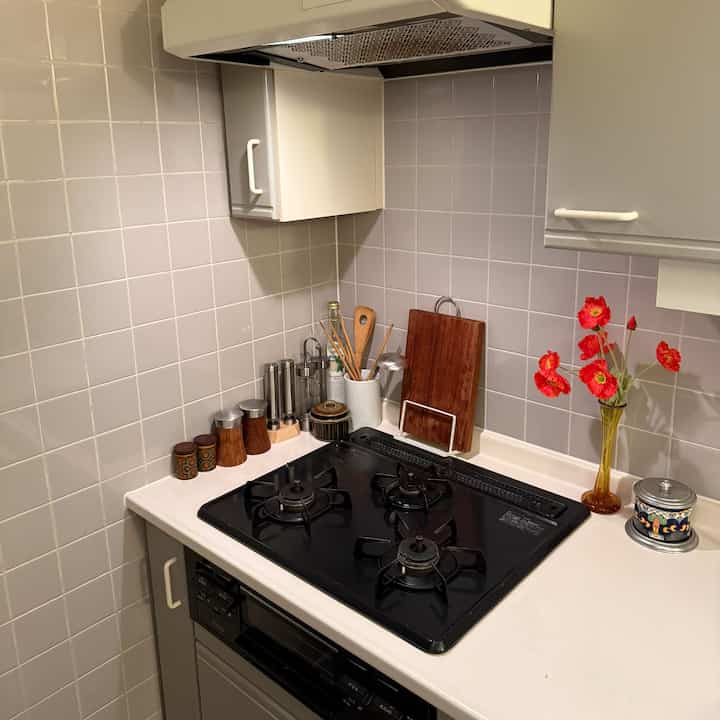 柔らかな色調と黒いガスレンジが配置された清潔感のあるキッチン、木製まな板と花瓶が調和するヴィンテージな雰囲気の空間