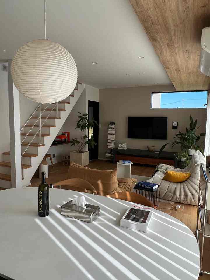 ウッドトーンと白を基調としたミッドセンチュリーモダンのリビング、くつろげるソファと大きなペンダントライトが配置された印象的な空間