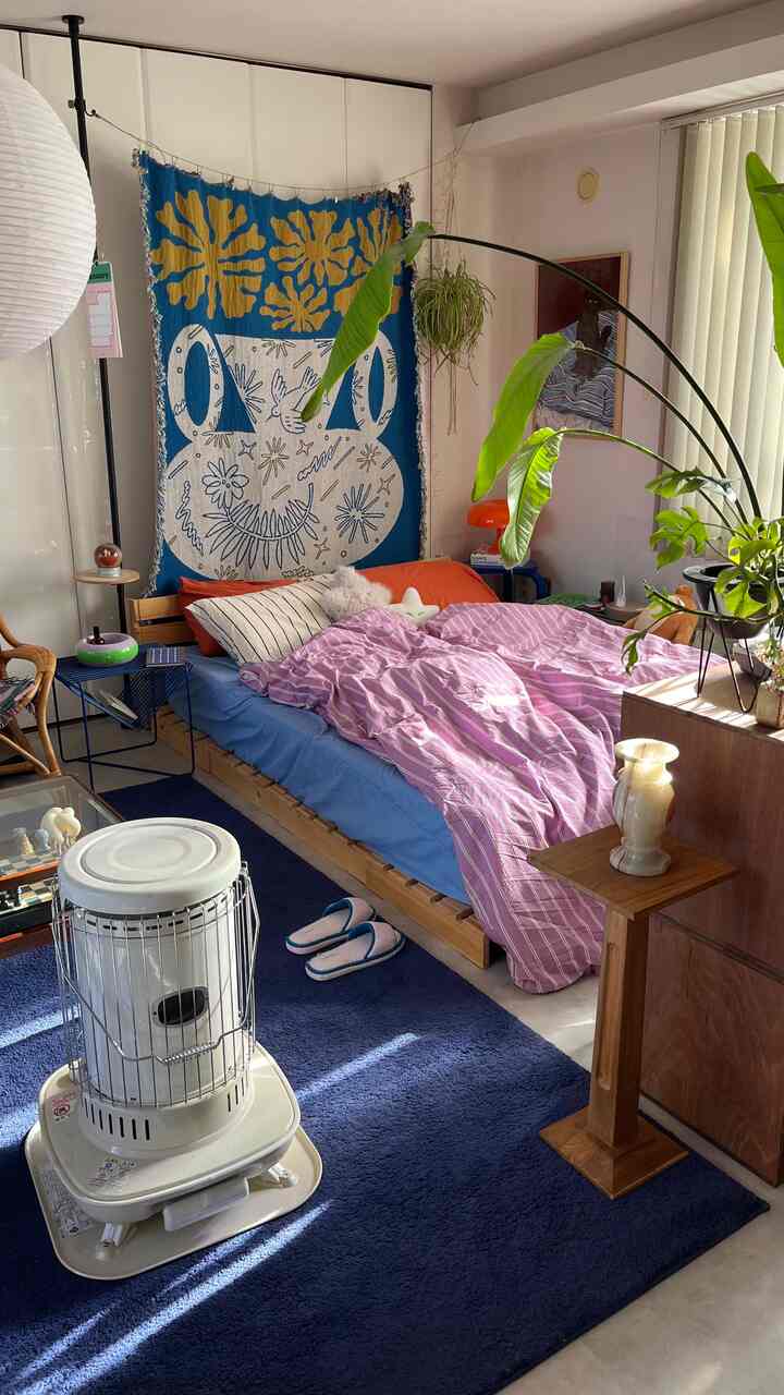 ピンクとブルーの色調が調和する寝室、木製ベッドとラタンチェア、多様な植物が配置された自然な雰囲気のインテリア