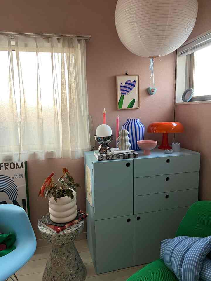 Natural living room with pastel pink walls and mint green cabinet, featuring decor items and plants creating a cozy atmosphere