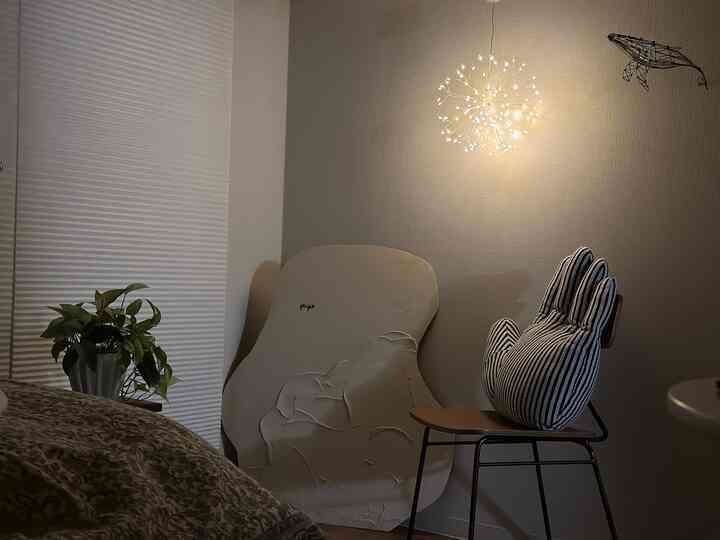 温かみのあるナチュラルトーンのリビングの一角、手の形のクッションとストリングライトが配された雰囲気のある空間