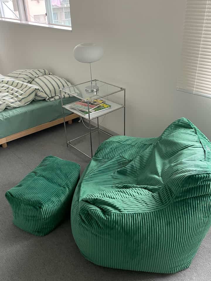 White-walled bedroom with green bedding and bean bag, designed for single occupant