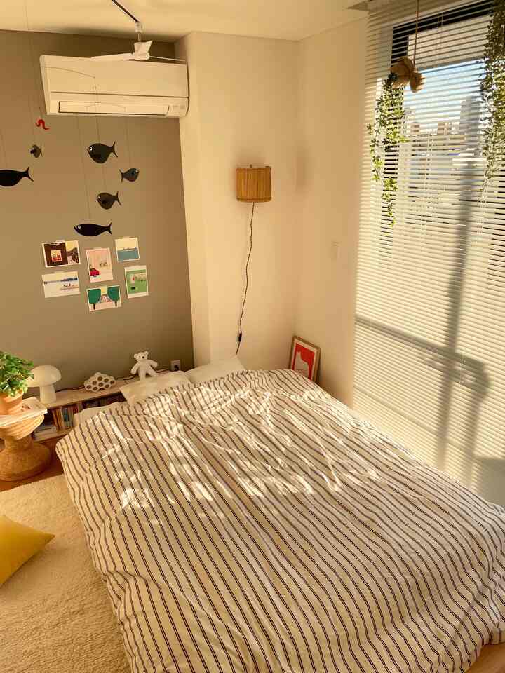 温かみのあるナチュラルカラーの北欧風寝室、ストライプの掛け布団カバーと白いブラインドが配された雰囲気のある空間