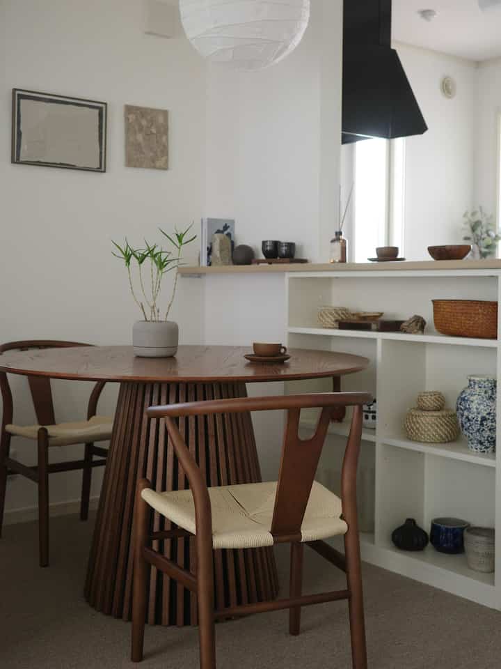 Natural wood tones and beige dining room featuring a round wooden table with green plant, clean and minimalist atmosphere