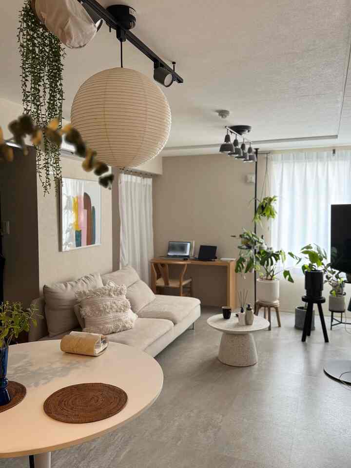 A modern living room in white and beige tones featuring a sofa, coffee table, and desk area with abundant natural light