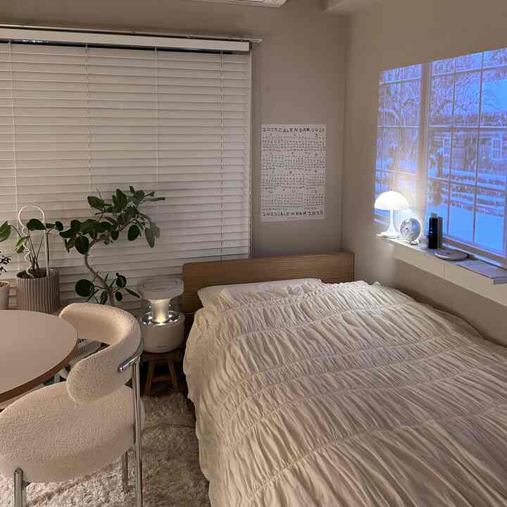 ナチュラルカラーとホワイトを基調とした寝室、ベッドとラウンドテーブルが配置され、プロジェクターで冬の景色を映し出す落ち着いた空間