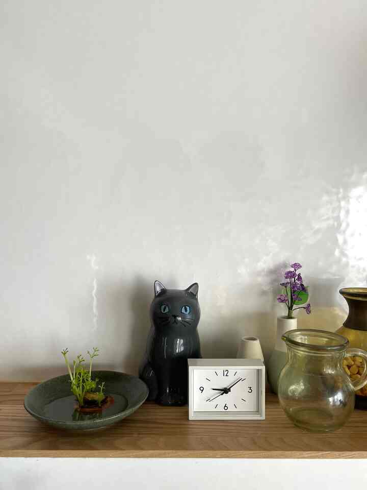 ナチュラルカラーのキッチン、木目調のカウンターに時計や猫型の花瓶が配置された雰囲気のあるインテリア