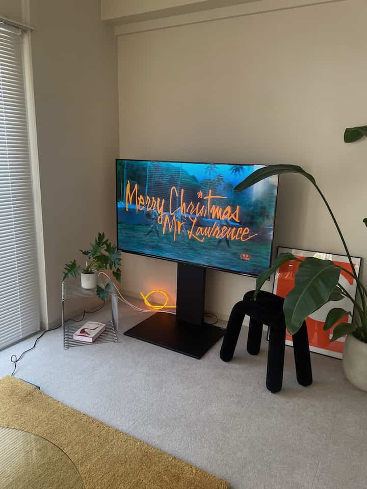 Modern living room with white walls and floor, yellow carpet, black stool, and green plants arranged neatly