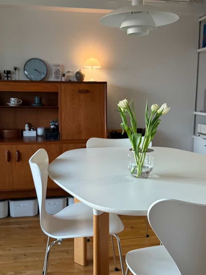 白とナチュラルな木目調の調和がとれたダイニングルーム、シンプルなテーブルと椅子、中央に花が飾られた透明なガラスの花瓶がある雰囲気のあるインテリア