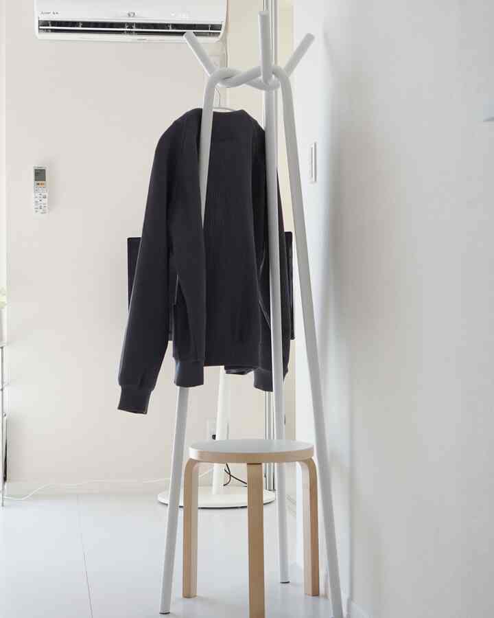 ホワイトトーンの玄関、白いコートハンガーと木製脚のスツールが配置されたシンプルでミニマルな雰囲気のインテリア