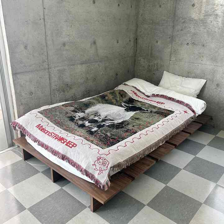Gray concrete walls and wood-toned bed frame with sheep-patterned blanket in a single bedroom space