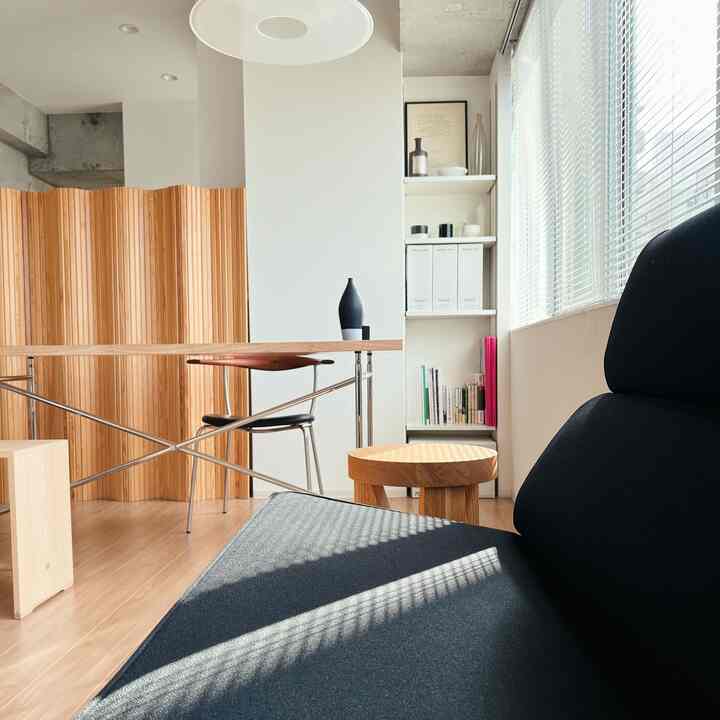 明るい白い壁とブラウンの木目調家具が調和したリビング、黒いソファと木製スツールが配置された自然な雰囲気のあるインテリア