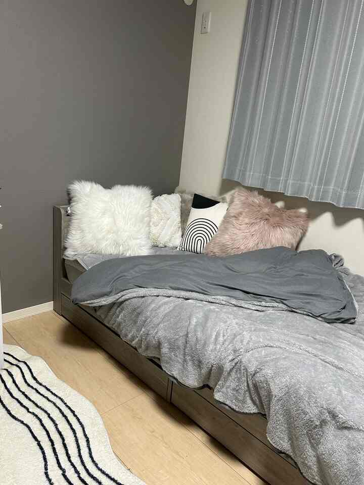 Gray-toned bedroom featuring a bed with assorted cushions, creating a simple and cozy interior atmosphere