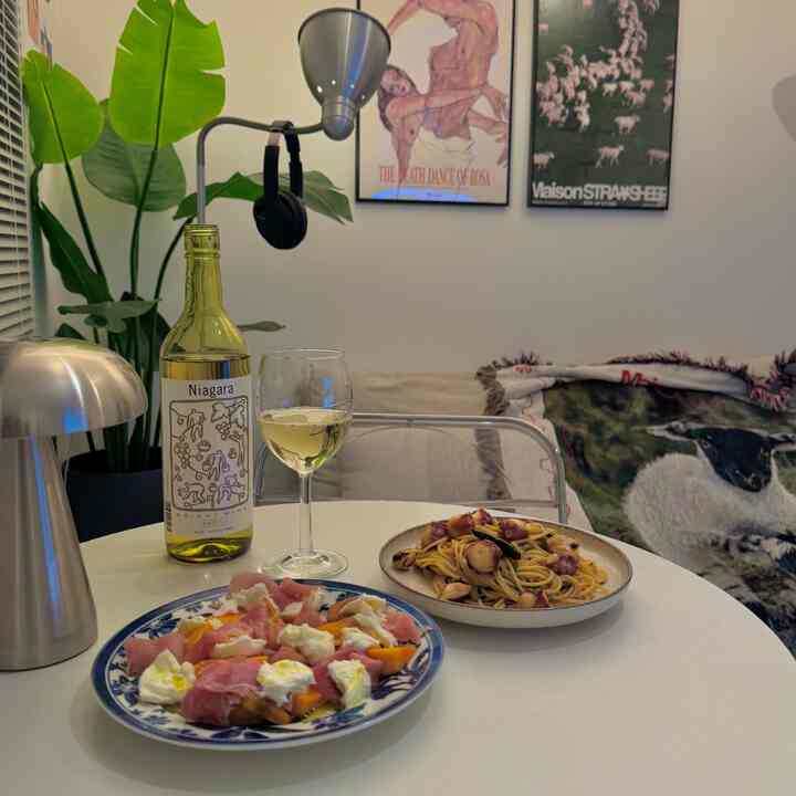 白を基調としたダイニング、テーブルにワインと2皿の料理が並ぶ落ち着いた一人暮らしの空間