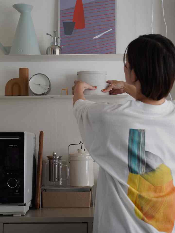 白とグレーのトーンのキッチン、棚に整頓された収納用品とポスターがあるミニマルな雰囲気のインテリア