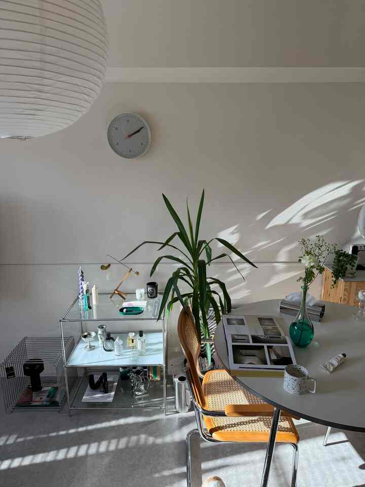 白と木目調が調和したリビング空間、ラウンドダイニングテーブルとモジュール式棚、観葉植物が配置された自然な雰囲気のインテリア