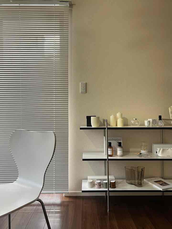 ホワイトとベージュのトーンでまとめられたワンルームのリビング、スツールと棚の上にキャンドルが置かれたナチュラルでシンプルな空間