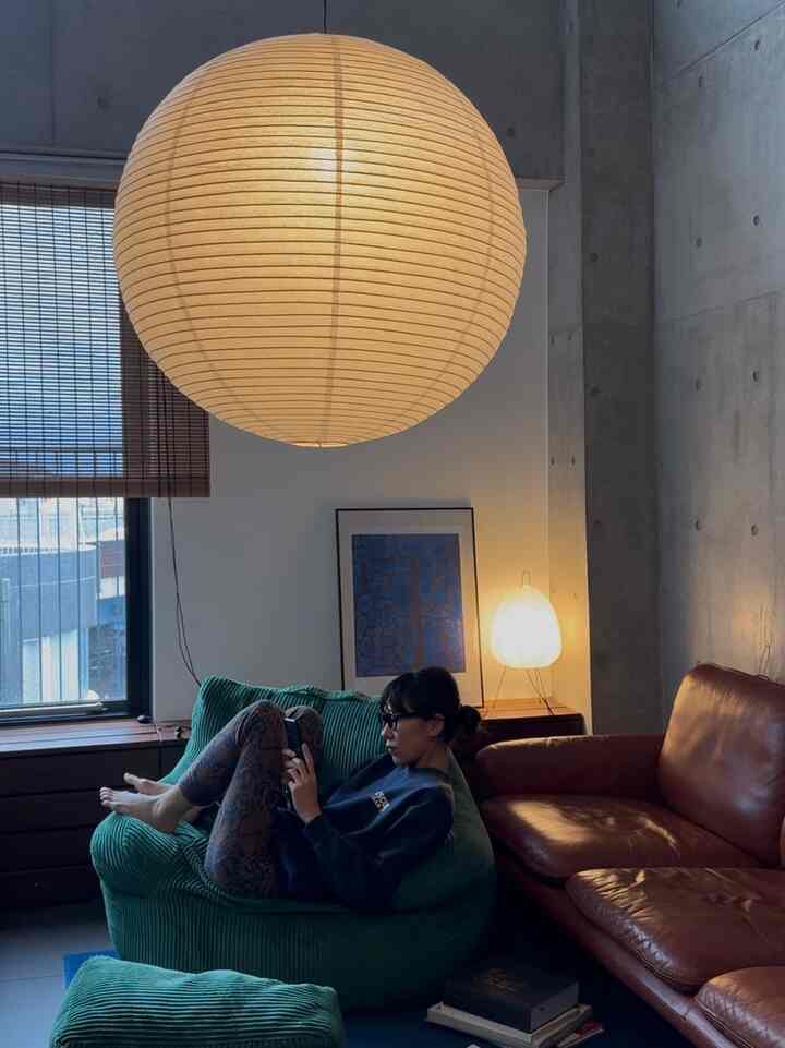 Mid-century modern living room in warm brown and green tones, featuring a large bean bag, leather sofa, and rice paper pendant light creating a cozy atmosphere