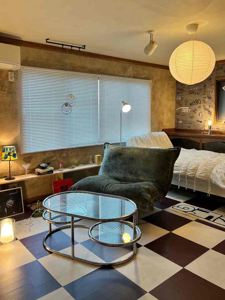 ヴィンテージ調の茶色い壁とチェック柄の床、緑のファブリックアームチェアとガラスのコーヒーテーブルが置かれたモダンなリビングルーム