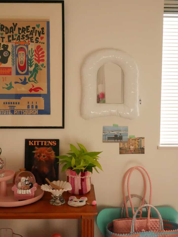 Beige-toned room with pink accents featuring mirror and plant on wooden table creating a cozy atmosphere