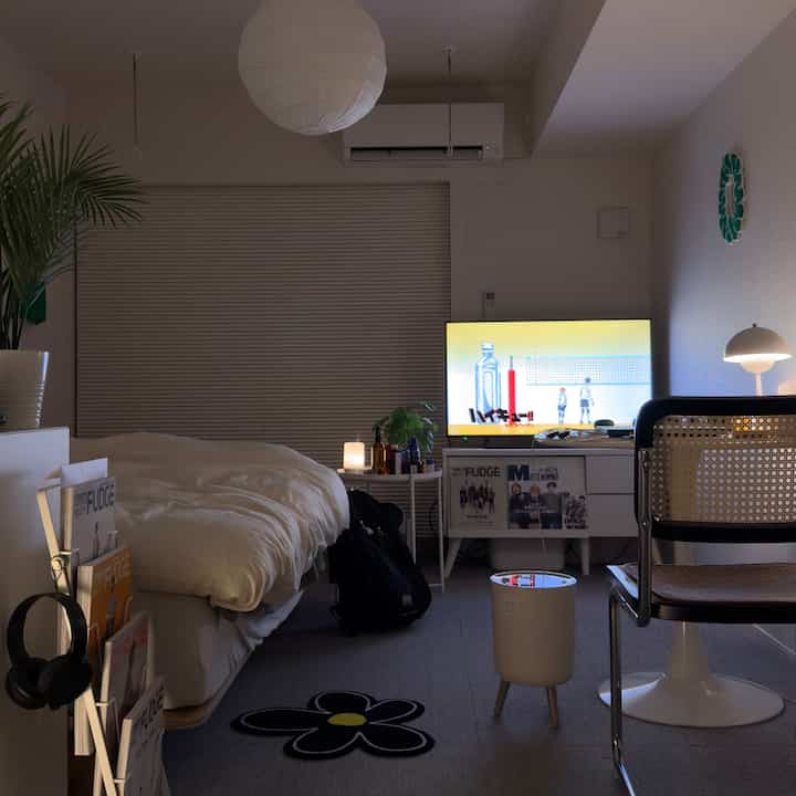 ホワイトとグリーンのトーンが調和した一人暮らしの寝室、モダンなデスクとテレビ台が配置されたシンプルで落ち着いた雰囲気のインテリア