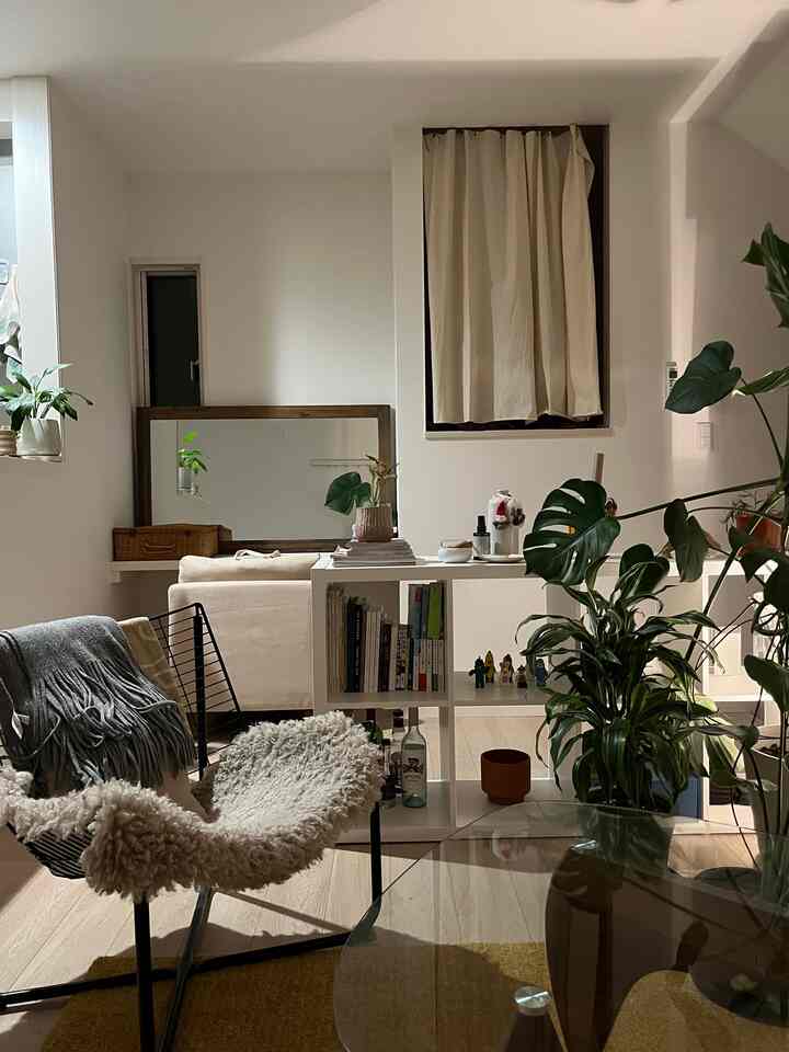 白い壁とベージュのソファ、棚、観葉植物が配置された落ち着いたリビングインテリア