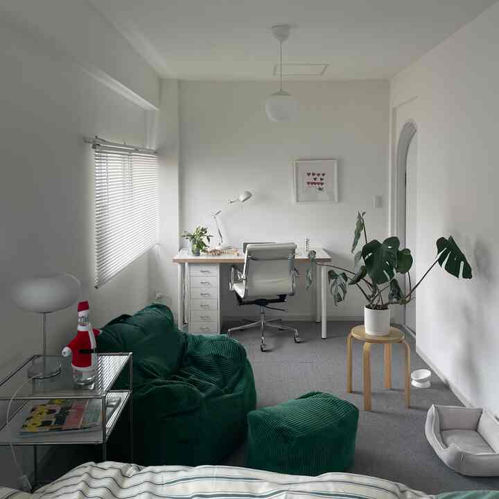 Modern home office with white walls and furniture, featuring a green bean bag sofa and large potted plant for a cozy feel