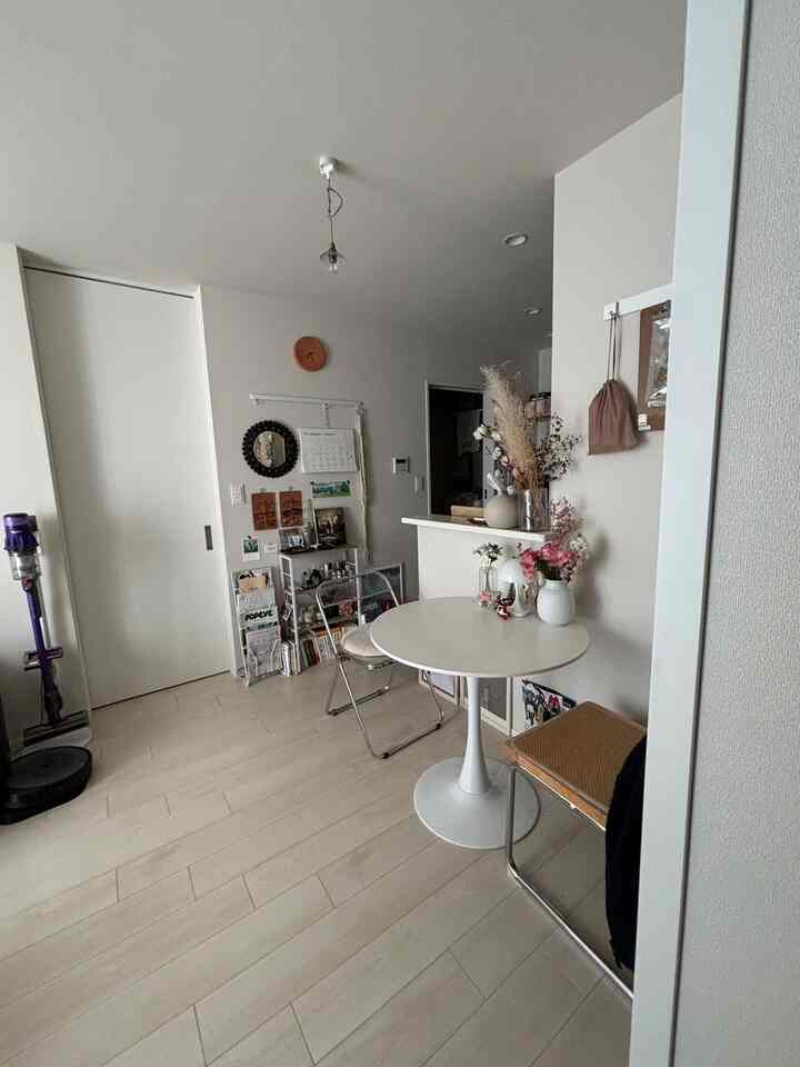 Bright white and natural wood-tone studio apartment living space featuring a round white table and chairs with a simple aesthetic