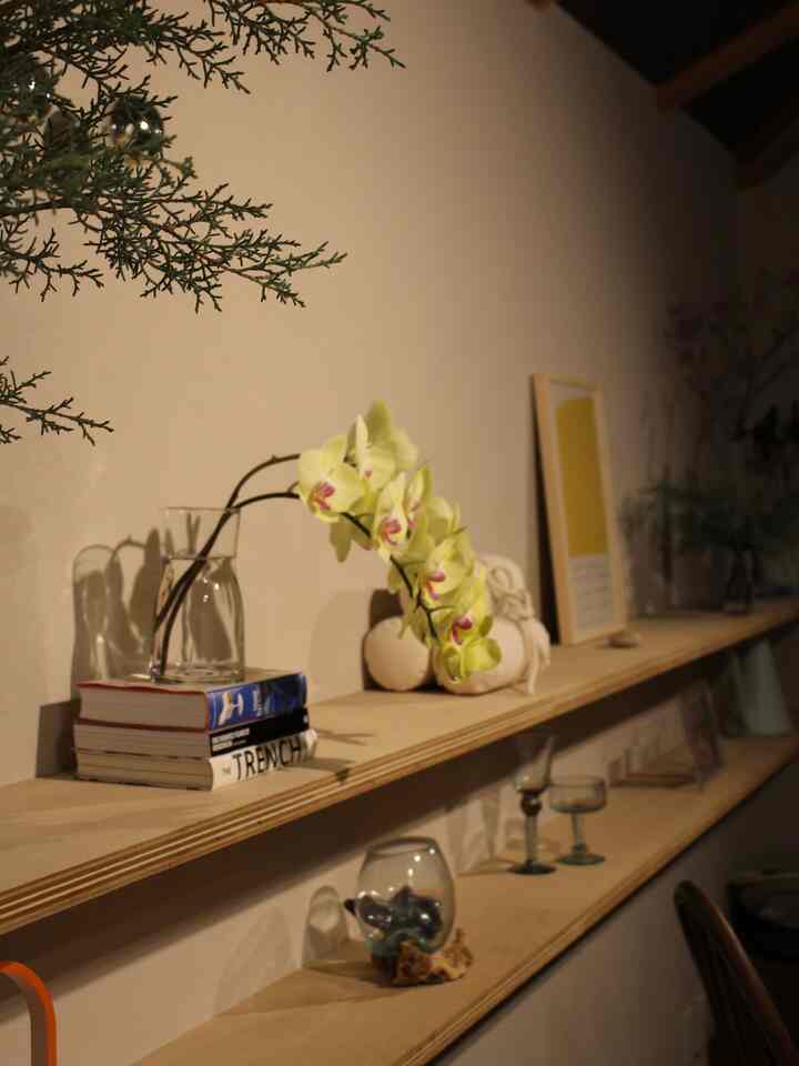 ベージュの壁とナチュラルな木製のウォールシェルフが設置されたダイニング、花瓶やポスター、オブジェが配置された雰囲気のあるインテリア