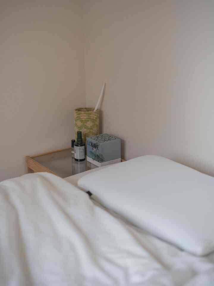 ナチュラルカラーの寝室、木製サイドテーブルと白い枕が置かれたシンプルな空間