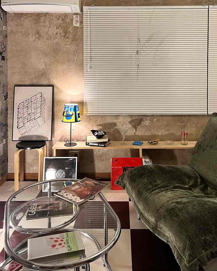 A beige natural-toned living room featuring a green sofa, vintage posters, and a checkerboard floor creating a cozy ambiance