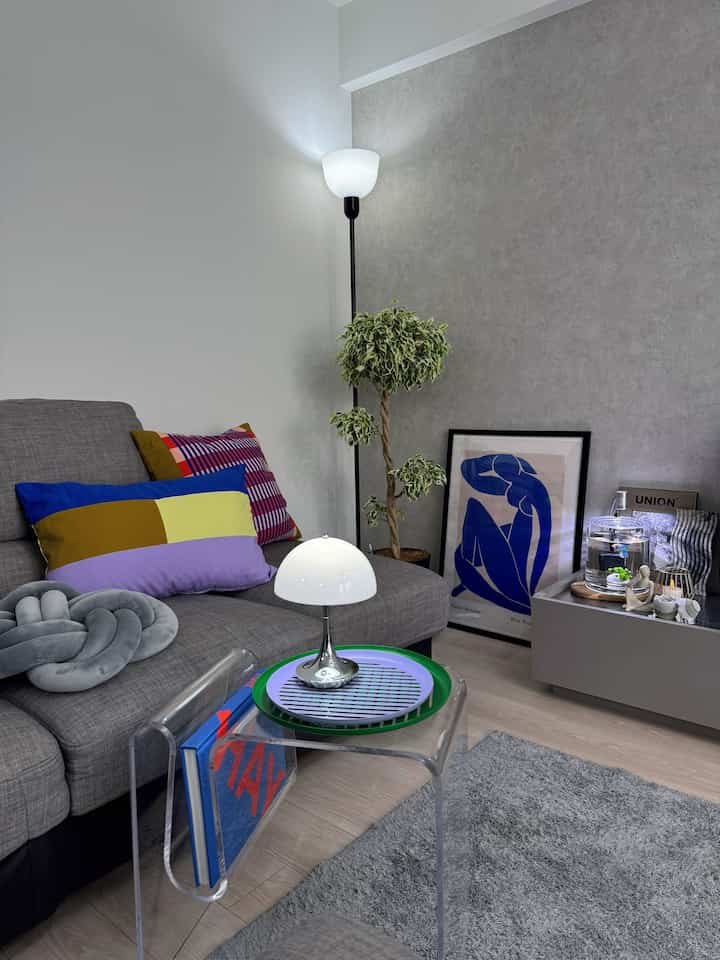 グレーのソファとカラフルなクッションが配された北欧風リビング、フロアランプと植物が調和するモダンで清潔感のあるインテリア