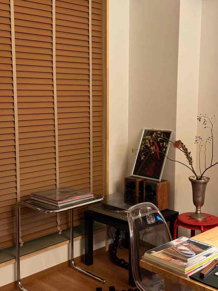 暖かみのあるブラウンの木目調とベージュの壁が調和した一人暮らし用のリビング、透明な椅子とサイドテーブル、ヴィンテージのターンテーブルが置かれた雰囲気のある空間