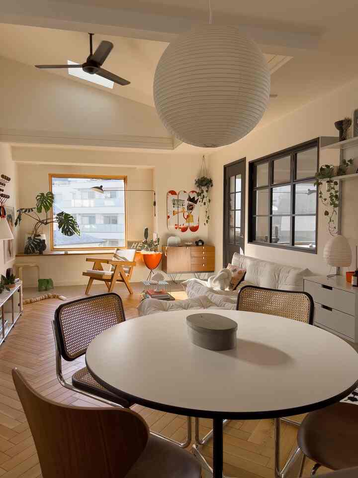 ナチュラルな色調のダイニングとリビング空間、丸いダイニングテーブルと木目調の椅子、クリーム色のソファが配置された雰囲気のあるインテリア