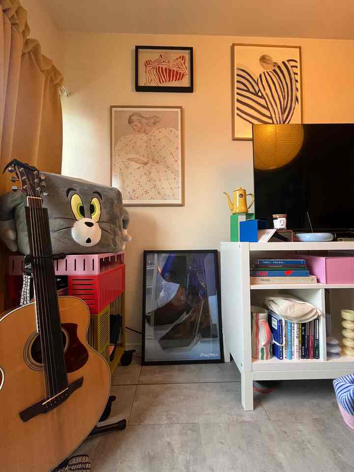 温かみのある色調のリビング、白い本棚と赤い収納ユニット、多彩なポスターとギターが配置された印象的なインテリア