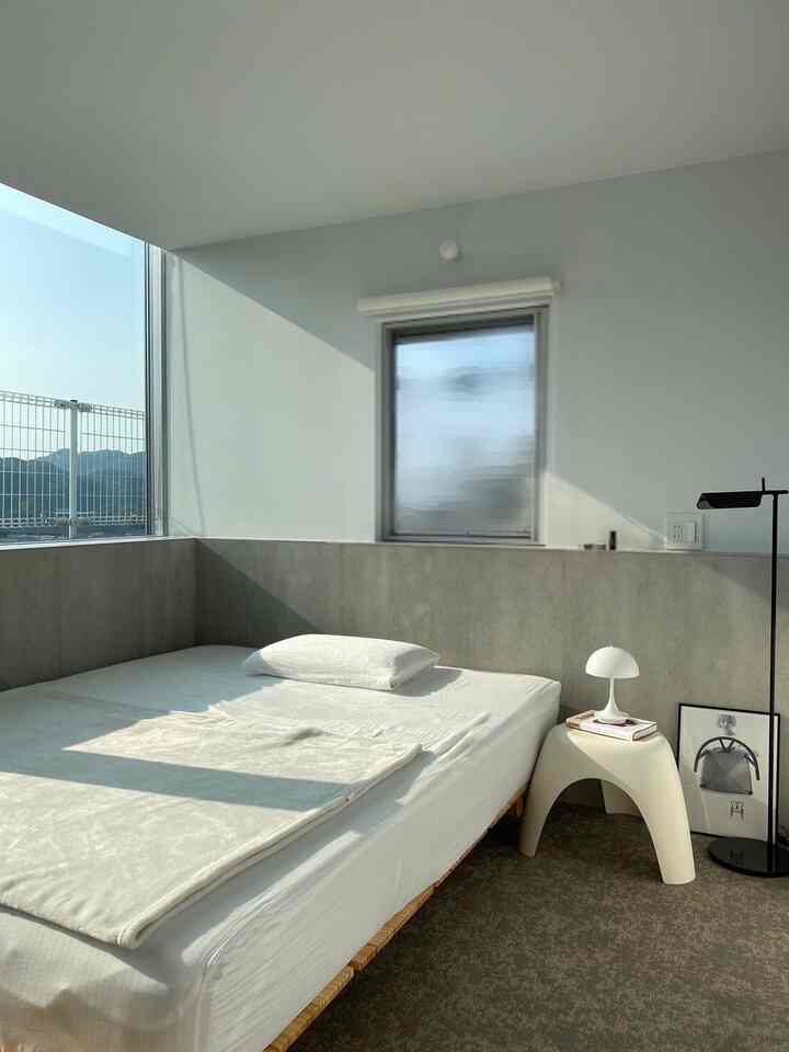 Bright white and gray tone half-basement bedroom featuring low ceiling, modern bed frame, and sleek lamps in a clean setting