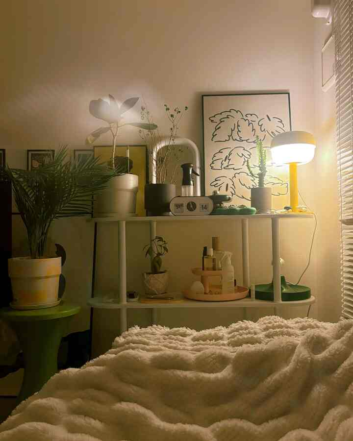Cozy bedroom with warm lighting, white walls and bed, featuring a shelf with plants and decor in a natural modern style