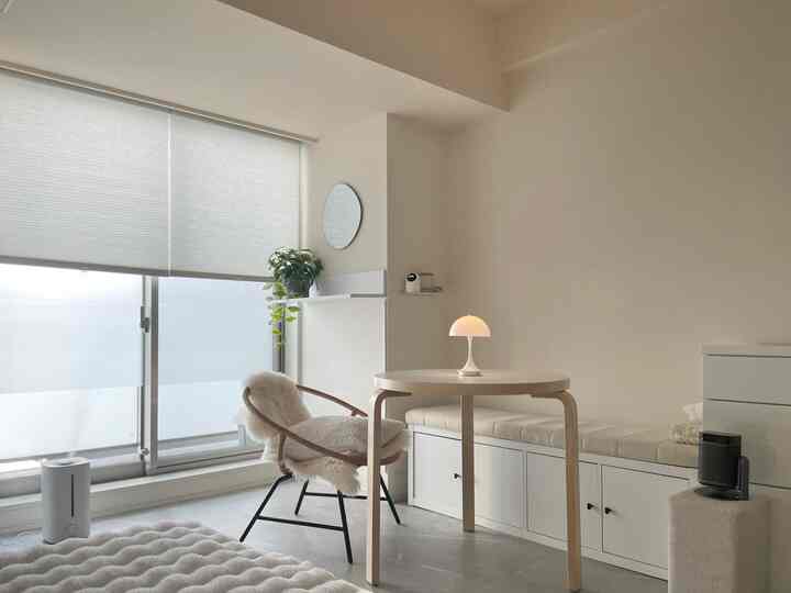 明るいホワイトとナチュラルカラーの北欧風リビング、丸いダイニングテーブルとクッション付きベンチが配置されたミニマルな空間