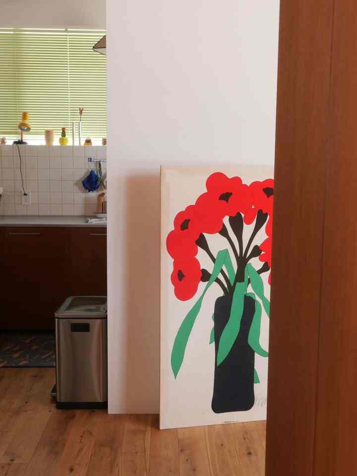 ナチュラルなブラウンの木目床と白い壁があるキッチンスペース、大きな赤い花のアートが壁にもたれかかっている印象的な空間