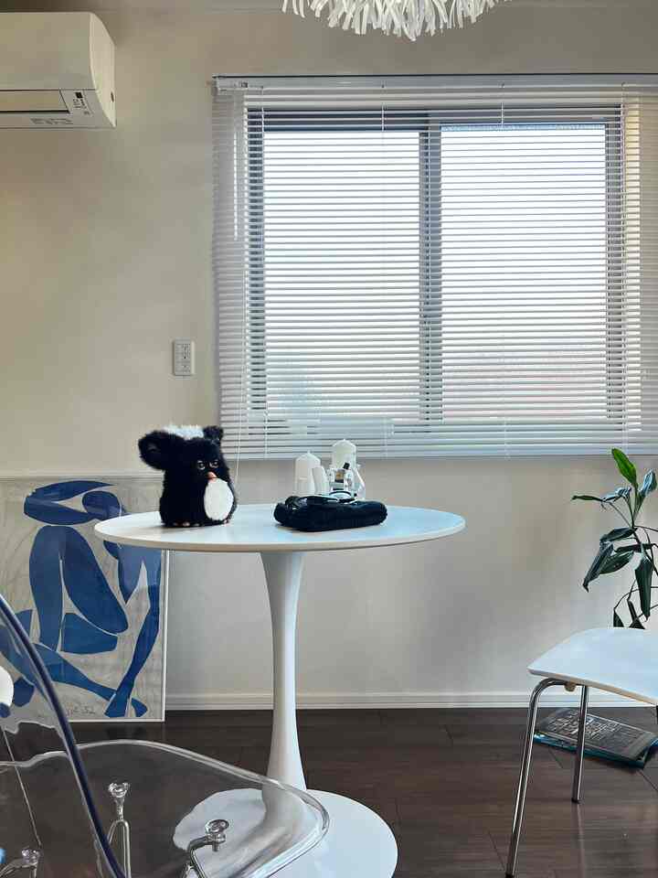 白と木目調の調和がとれたダイニング、丸テーブルとブラインドが配置されたシンプルなカフェ風のインテリア