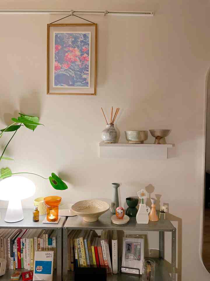 Natural beige-toned 1K single household space with metal shelf, earthy ceramic decorations, and warm table lamp lighting