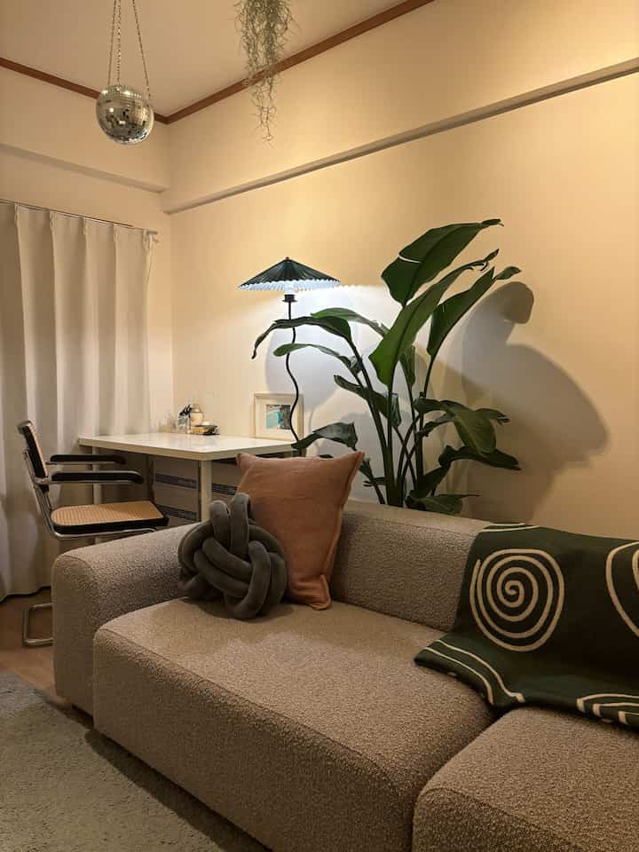 ベージュとグリーンのトーンが調和した2LDKのリビング、クッションと観葉植物が配置されている印象的なシンプルモダンインテリア