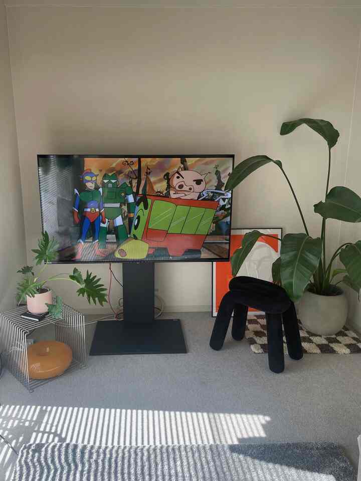 白い壁とグレーのラグがあるモダンなリビング、テレビスタンドと植物が配置された落ち着いた雰囲気のインテリア