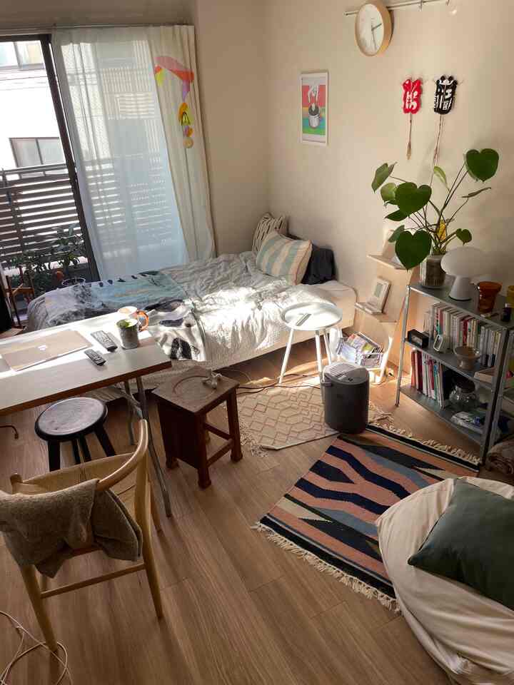 木目調の床と白い壁のワンルーム、ベッド・デスク・棚が配置された居心地のよい一人暮らしの空間