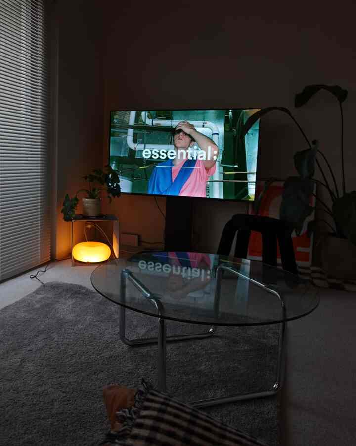 A modern and minimal living room with warm lighting and plants, featuring a glass coffee table centrally placed in a cozy atmosphere