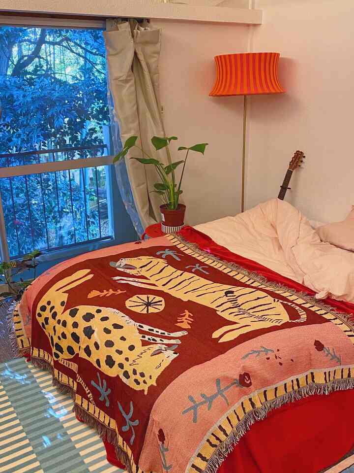 ピンクの寝具と動物柄の掛け布団カバーがあるワンルームの寝室、温かみのあるオレンジのフロアランプと自然光が入る窓が配された雰囲気のあるインテリア