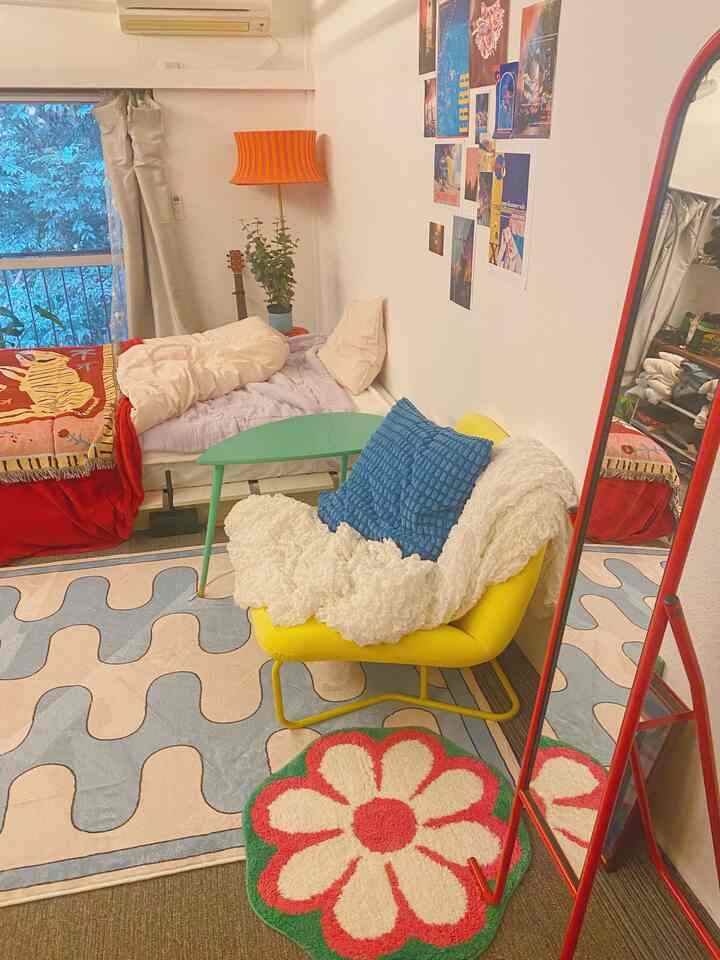 カラフルな色彩のワンルーム、黄色いアームチェアとピンクの寝具、緑のコーヒーテーブルが配置された雰囲気のあるインテリア