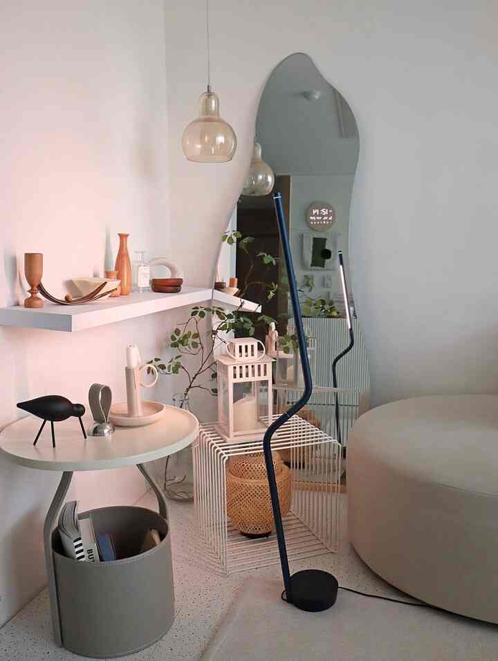 Soft white and ivory toned living room corner featuring wall shelf, pendant light, and an irregular large mirror with natural modern style