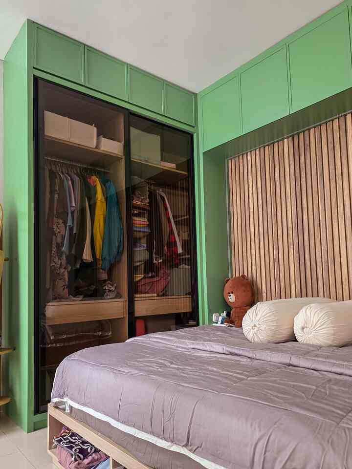 Simple modern bedroom in green tones featuring a bed with light purple bedding and wood-paneled wall, plus a glass-door closet