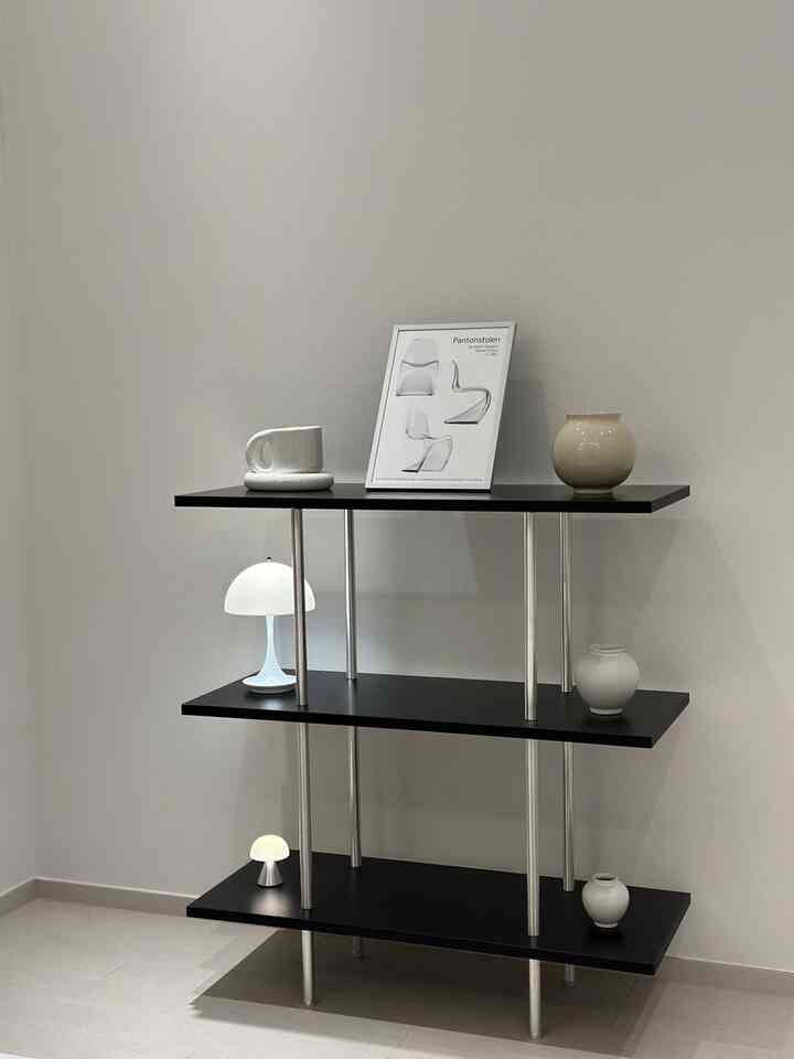 ナチュラルカラーの壁に黒い棚が配されたミニマルなリビング、白い花瓶とテーブルランプを配置したインテリア